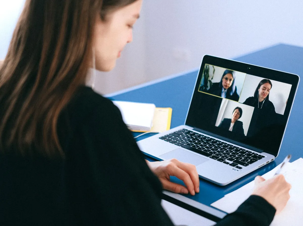 Mulher com fone de ouvido faz anotações diante de notebook com três entrevistadoras em videochamada