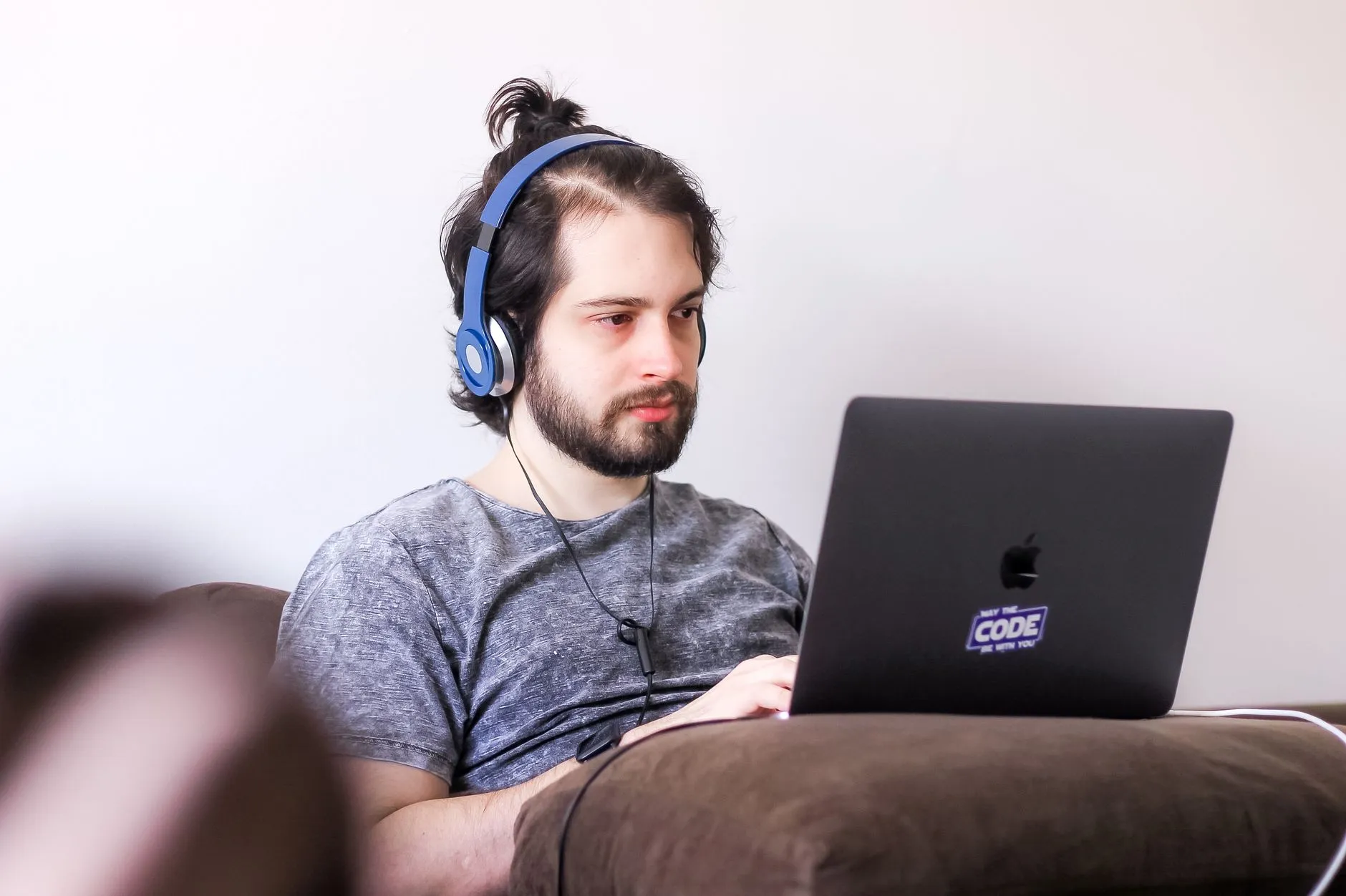 Homem de fones de ouvido trabalhando em um notebook no sofá